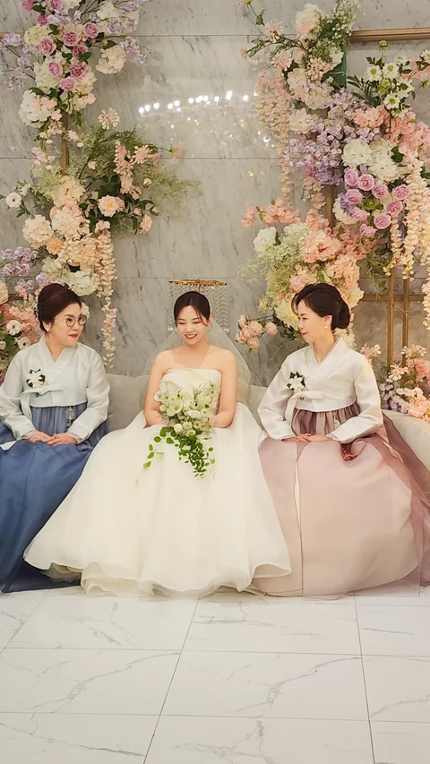 한복을 갖춰 입은 양가 어머님 사이에 앉아 함께 웃는 신부