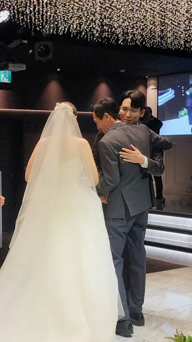 베일을 쓴 신부가 뒤에서 다가온 사람과 끌어안는 뒷모습
